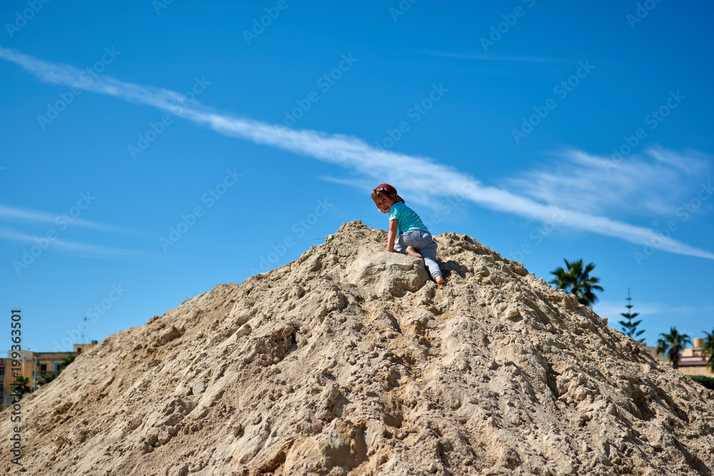 A child climbs up a mountain of sand on the beach