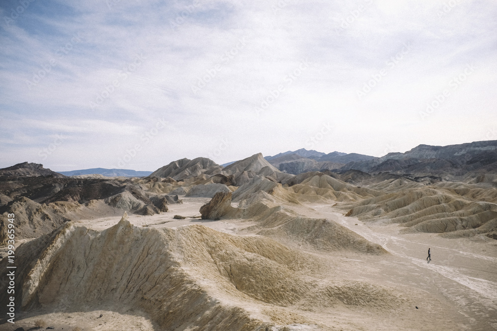 Mid distance view of hiker amidst desert against cloudy sky at Death Valley National Park Mid distance view of hiker amidst desert against cloudy sky at Death Valley National Park