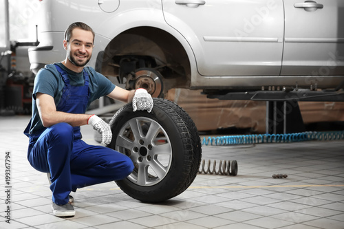 Young mechanic with car tire in service center © New Africa