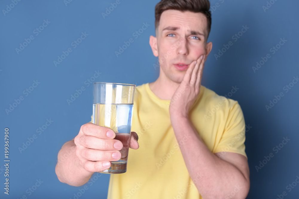 Young man with sensitive teeth and glass of cold water on color background Young man with sensitive teeth and glass of cold water on color background