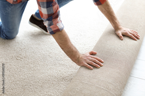 Fotografie Man rolling out new carpet flooring in room