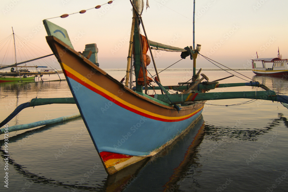 Balinese Fishing Boats Anchored in the Village of Pemuteran. Balinese fishing boats, called jukung, in the bay of northwest Bali, Indonesia during a beautiful sunrise. Balinese Fishing Boats Anchored in the Village of Pemuteran. Balinese fishing boats, called jukung, in the bay of northwest Bali, Indonesia during a beautiful sunrise.