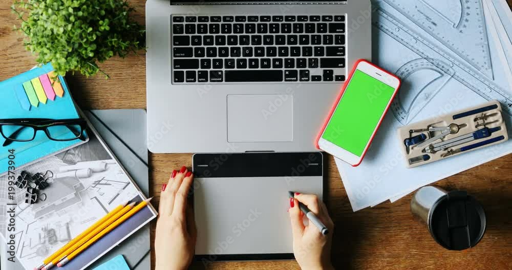 top view of female designer drawing sketches on graphic tablet closeup top view smartphone green screen chromakey laptop keyboard art space business design freelance mockup text content sketch app