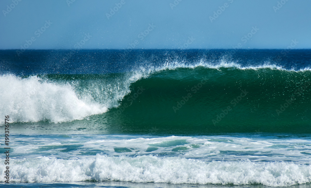Clean and clear curling wave breaks onto beach on sunny day, front on photo coastal Australia.