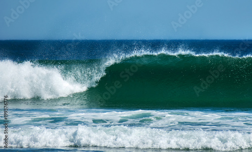 Clean and clear curling wave breaks onto beach on sunny day, front on photo coastal Australia.