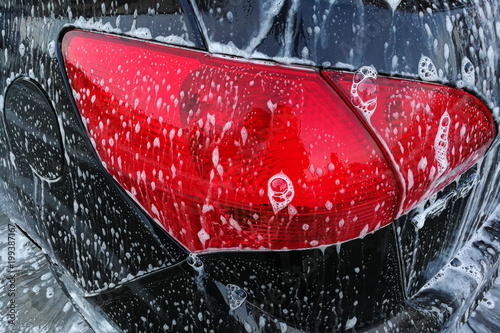 Detail photo of brown car rear red light covered with soap foam when being cleaned in carwash. © Lubo Ivanko