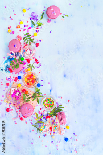 Pink macarons, candies, confetti and sprinkles in a creative party vignette with copy space. Colorful celebration flat lay.