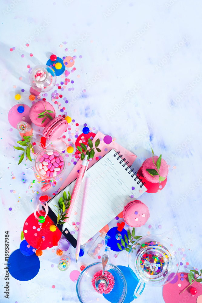 Party management and organization concept with sweets, confetti and an open notepad with blank pages. Creative celebration flat lay with copy space.