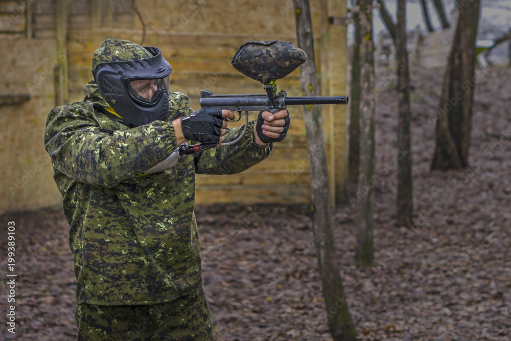 Fototapeta premium Paintball player takes aim, hides and shooting. Man wearing protective equipment