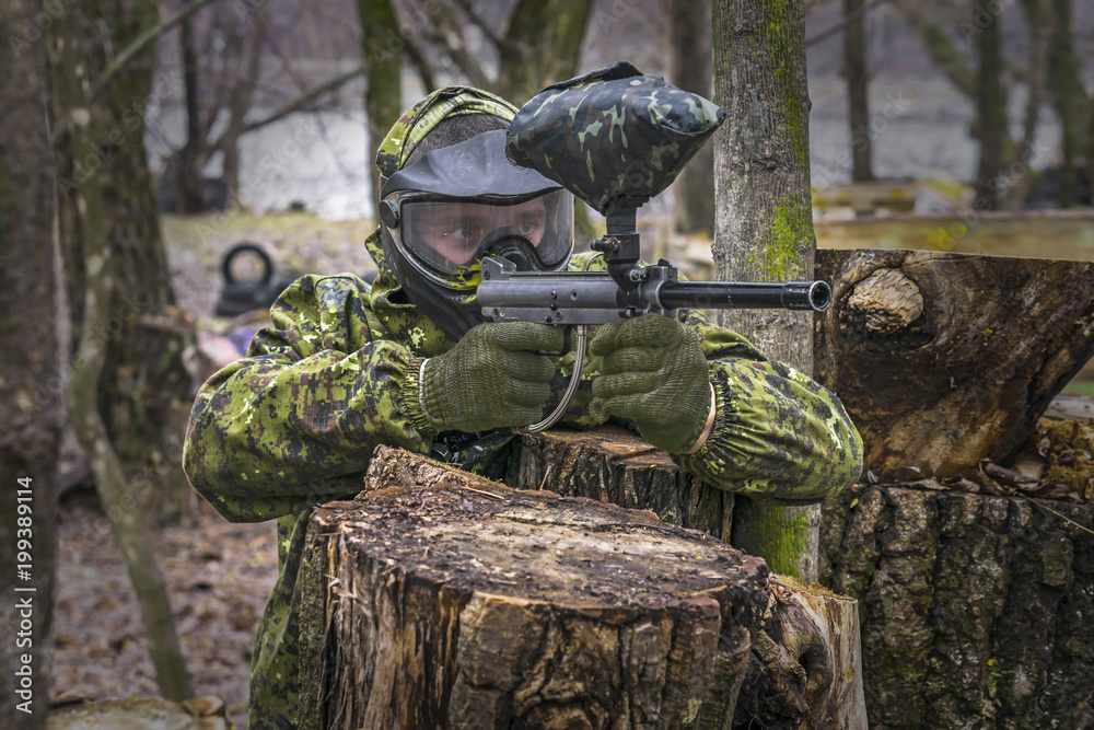 Obraz premium Paintball player takes aim, hides and shooting. Man wearing protective equipment