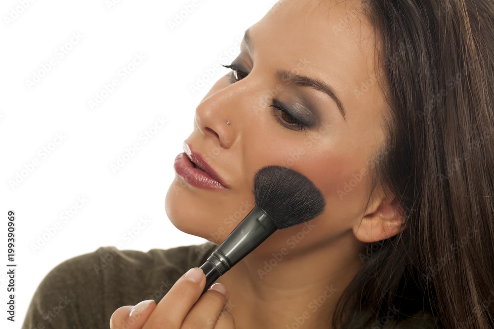 Beutiful young woman applying blush with a brush on white background Beutiful young woman applying blush with a brush on white background