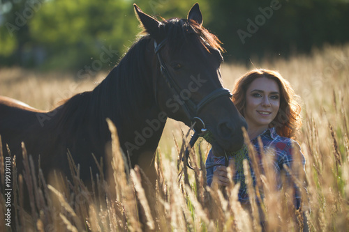 Portrait of a young woman and horse in the meadow at sunny summer
