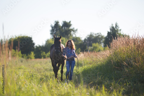 Young woman walking with the horse in meadow at summer day © KONSTANTIN SHISHKIN
