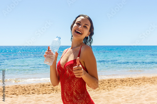 happy tanned girl holding a water bottle gesturing thumbs up on the beach photo