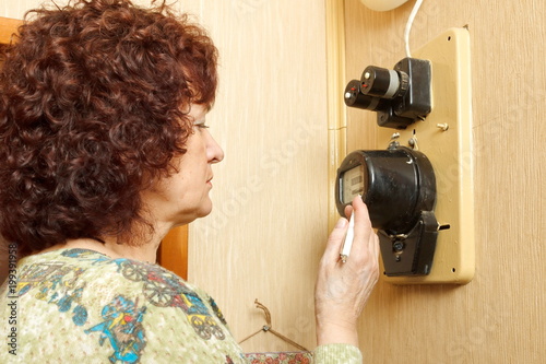 The woman takes the indications of the apartment electric meter and writes it into the notebook photo