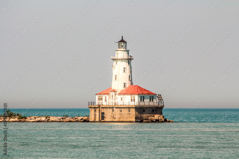 Lighthouse in the middle of the lake in a sunny day. Sunny day, in the middle of the lake there is a lighthouse with a narrow walkway to the land, cyan water surrounds the small lighthouse island. Lighthouse in the middle of the lake in a sunny day. Sunny day, in the middle of the lake there is a lighthouse with a narrow walkway to the land, cyan water surrounds the small lighthouse island.
