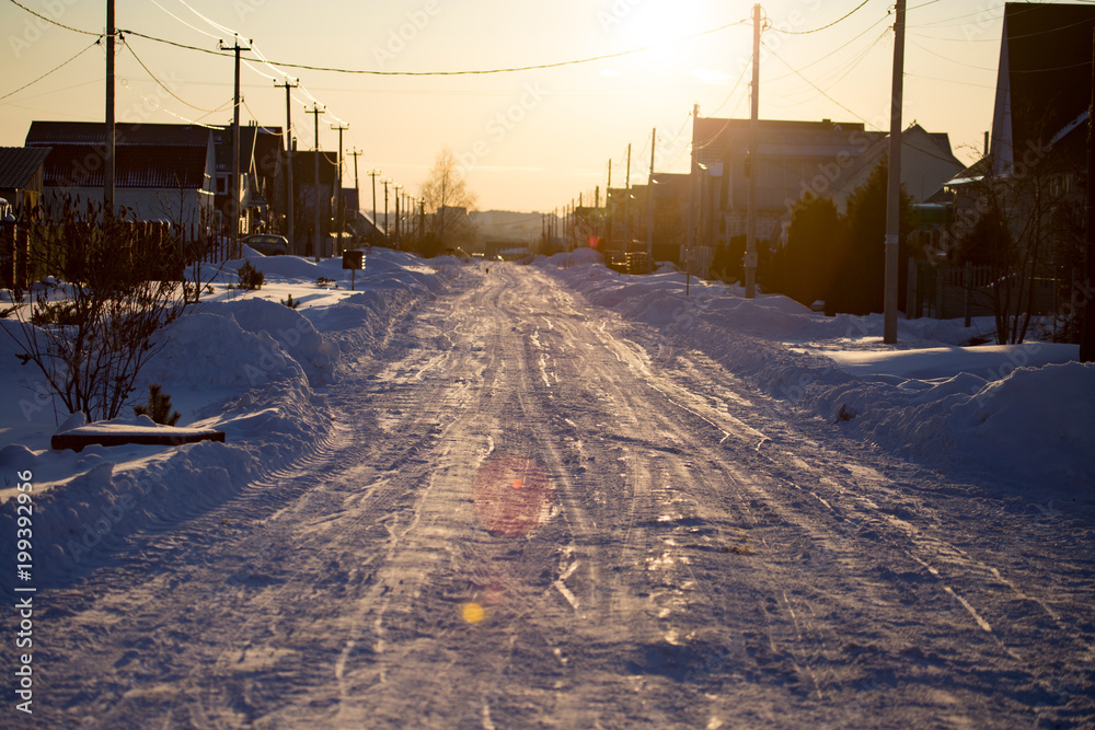 Road in the snow in the village at sunset