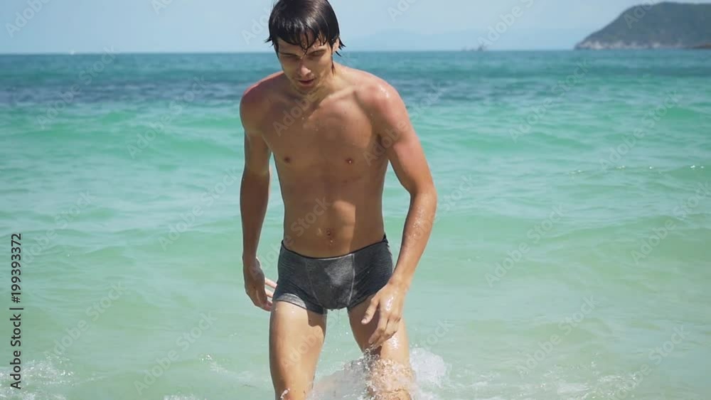 Attractive young man swimming into the sea and splashing waves in slow motion. Sexy guy looks at camera. happy summer vacation concept. 1920x1080