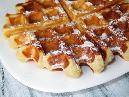 Belgian waffles in a white plate on a table. Wafer in sugar powder