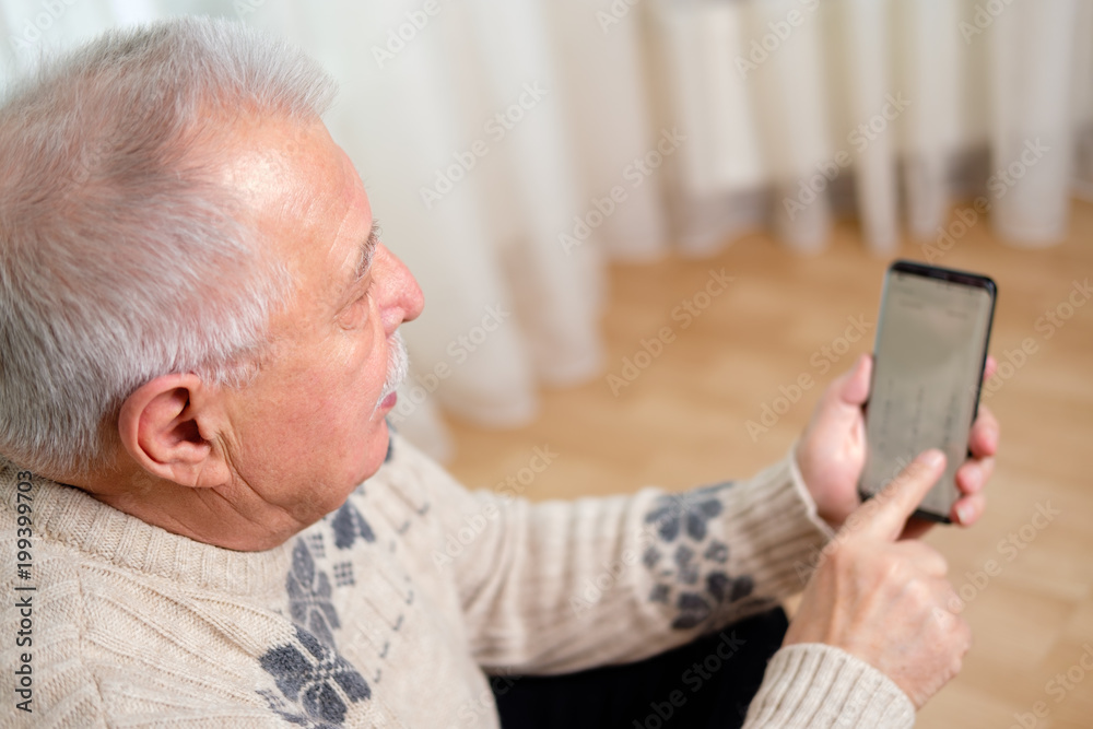 Old senior man dialing phone number and texting on smartphone at home sitting in armchair. technology, lifestyle and communication concept Old senior man dialing phone number and texting on smartphone at home sitting in armchair. technology, lifestyle and communication concept