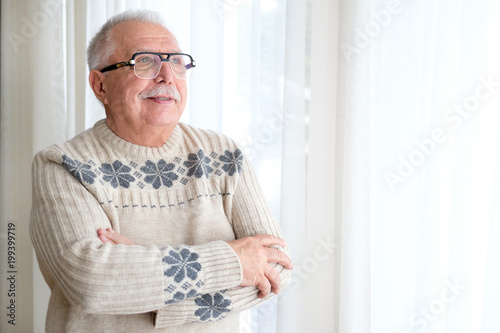 Old age, lifestyle and people concept - close up of pensive senior man in glasses looking into window at home