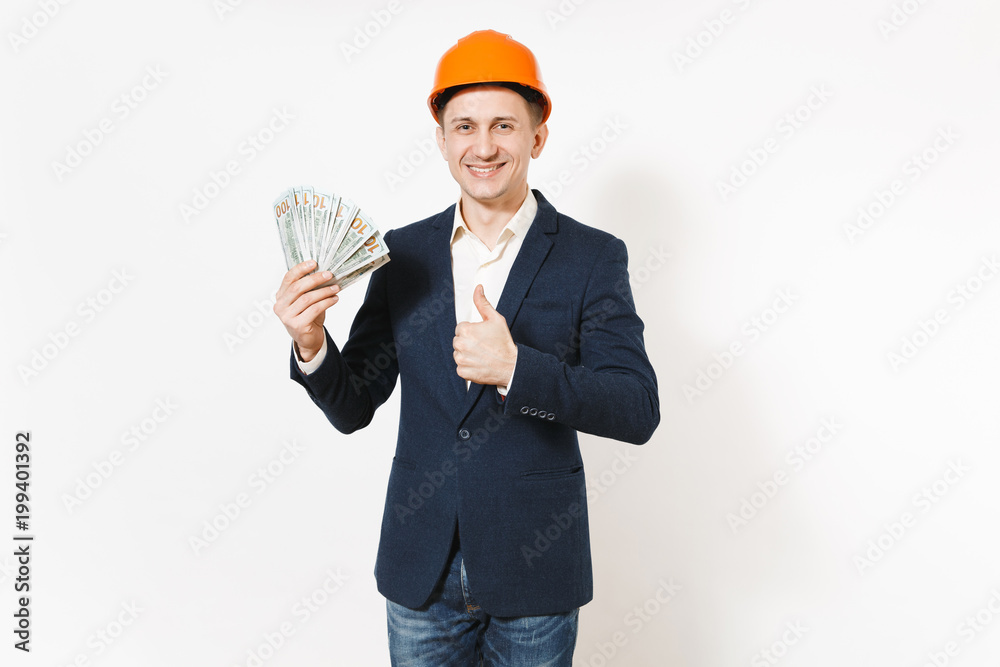 Young smiling businessman in dark suit, protective hardhat holding bundle of dollars, cash money and showing thumb up isolated on white background. Male worker for advertisement. Business concept. Young smiling businessman in dark suit, protective hardhat holding bundle of dollars, cash money and showing thumb up isolated on white background. Male worker for advertisement. Business concept.