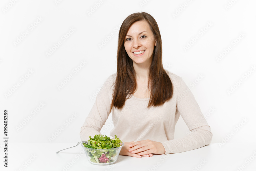 Young woman sitting at table with green leaves salad in glass bowl isolated on white background. Proper nutrition, vegetarian food, healthy lifestyle, dieting concept. Advertising area with copy space Young woman sitting at table with green leaves salad in glass bowl isolated on white background. Proper nutrition, vegetarian food, healthy lifestyle, dieting concept. Advertising area with copy space
