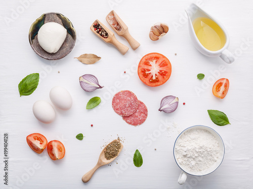 Fototapeta Naklejka Na Ścianę i Meble -  The ingredients for homemade pizza with ingredients sweet basil ,tomato ,garlic ,bay leaves ,pepper ,onion and mozzarella cheese on white wooden background with flat lay.