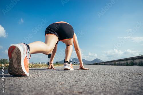 An asian woman athletic is jogging on the concrete road, she is warming her body and tideten her tying her shoes tightly fitting before workout.
