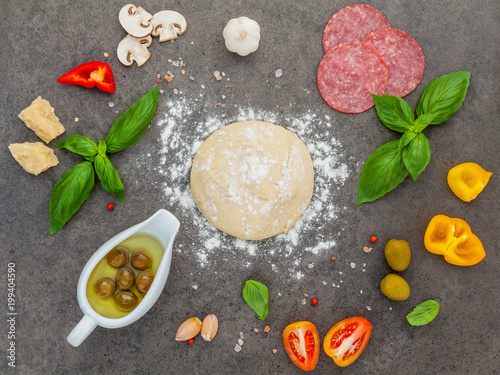 The ingredients for homemade pizza with ingredients sweet basil ,tomato ,garlic ,bay leaves ,pepper ,onion and mozzarella cheese on dark stone background with flat lay.