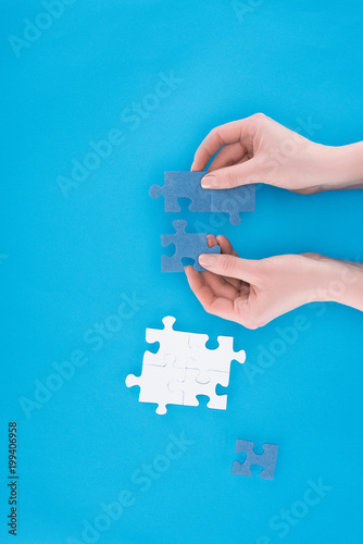 cropped image of businesswoman assembling blue puzzles isolated on blue, business concept