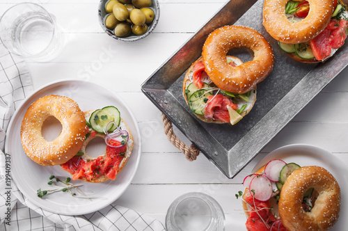 Bagels with salmon fish, cream cheese, cucumber and fresh radish slices on metallic tra on white wooden background photo