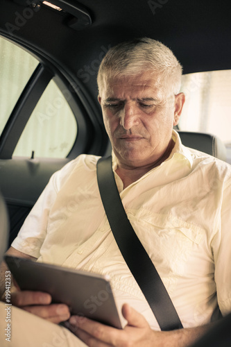 Business man using digital tablet and reading document. Senior man working in taxi.