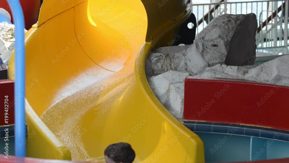 Child cheerfully slides down yellow water slide into a small pool