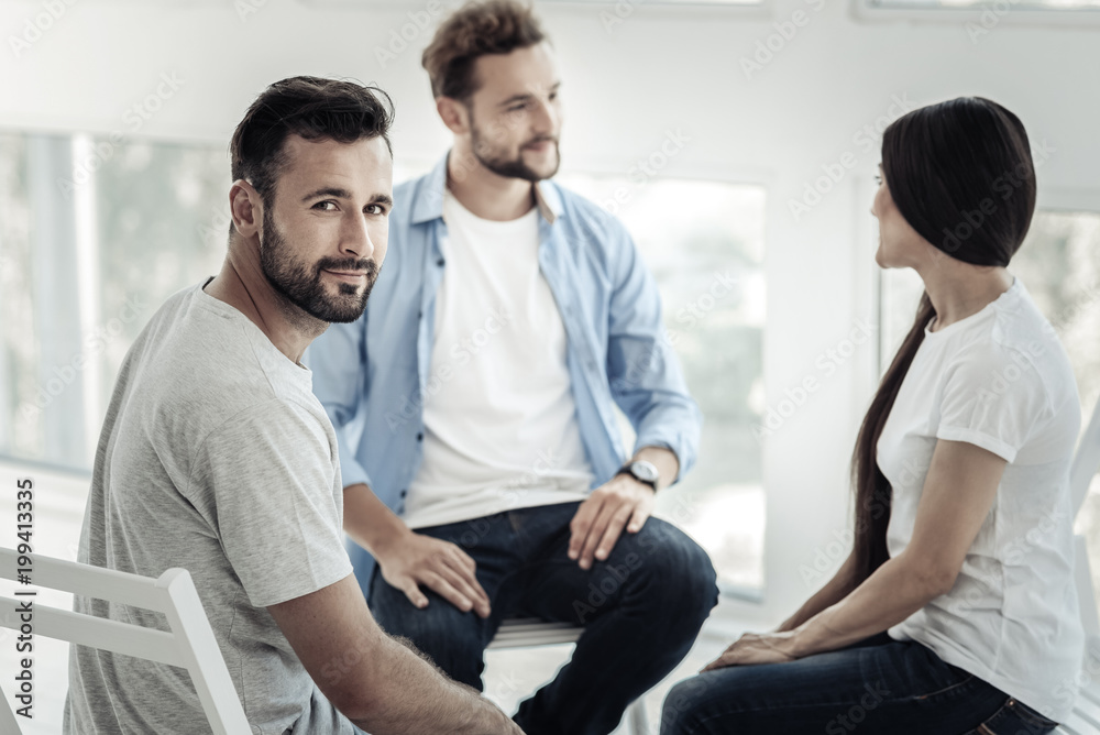 Obraz premium Positive mood. Nice positive cheerful man smiling and looking at you while visiting psychological session