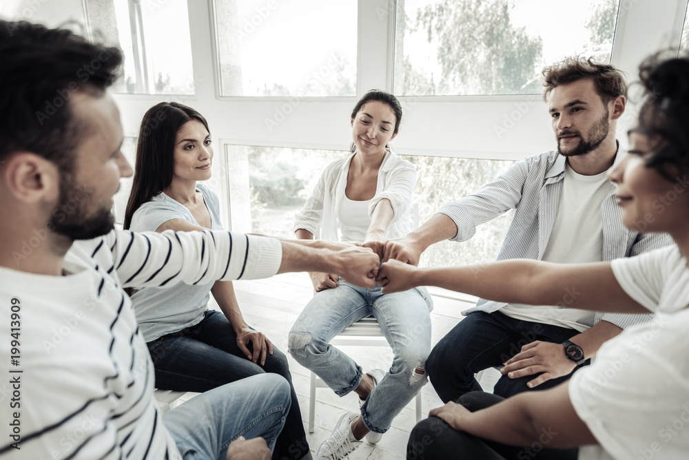 We are the team. Positive joyful young people sitting in the circle and putting their hands together while being a team We are the team. Positive joyful young people sitting in the circle and putting their hands together while being a team