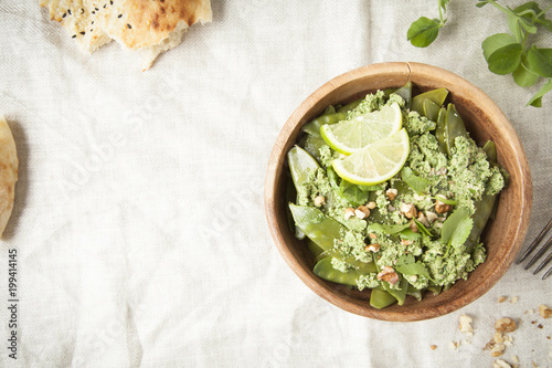 Green peapods with pesto sauce in wooden bowl on rustic background.