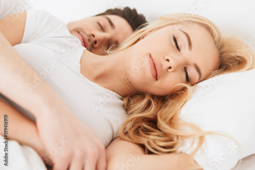 Loving couple lies in bed sleeping indoors at home.