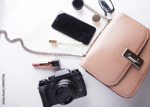 Top view of woman beige bag with accessories smartphone, cosmetics, lasses, camera and perfume on white background.