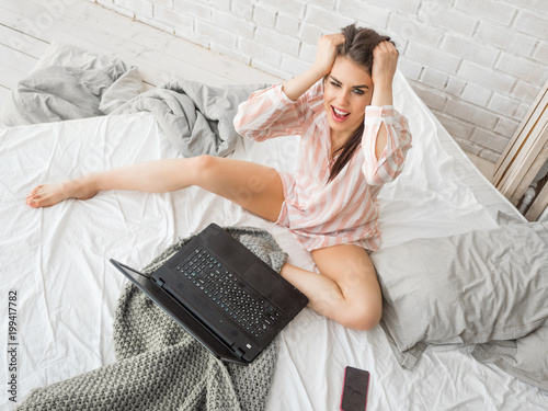 Young woman shoked looking in laptop sitting in the bed photo