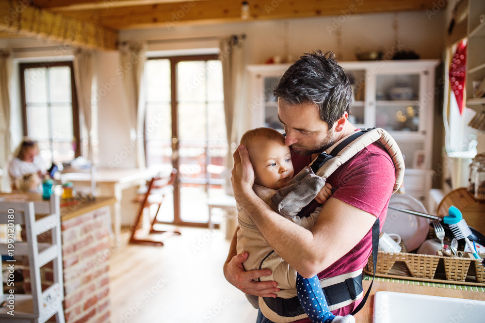 Father with a baby girl in a carrier at home.
