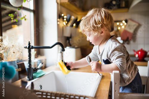 A toddler boy washing up the dishes.