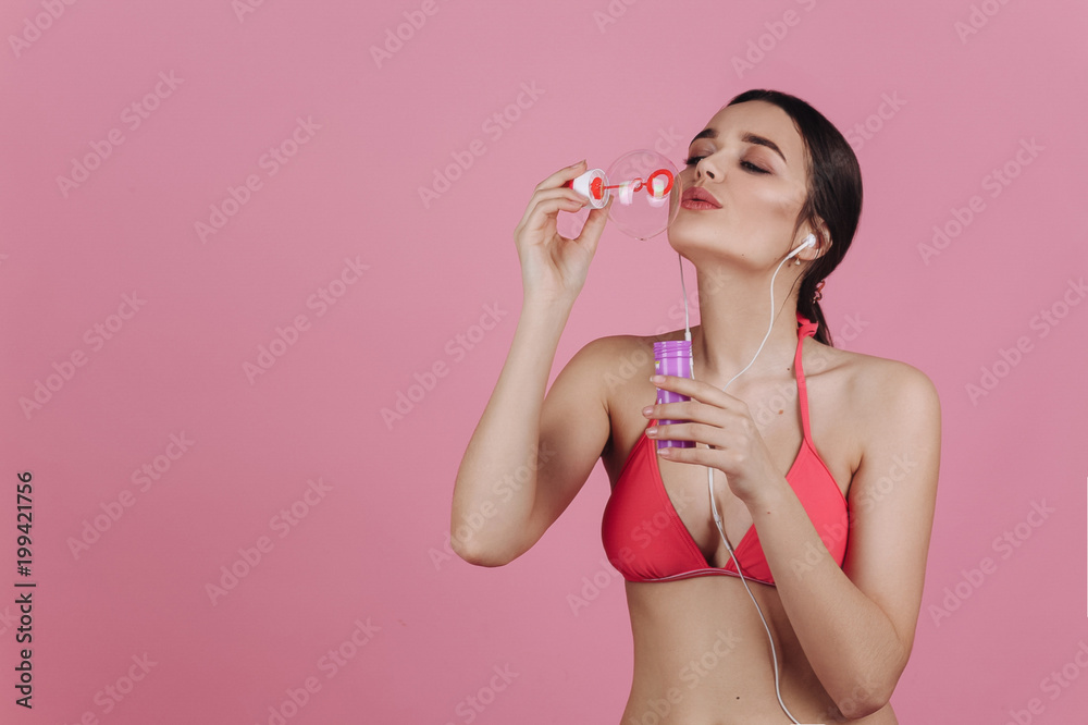 Girl in pink bikini makes soap balloons stand in with earphones Girl in pink bikini makes soap balloons stand in with earphones