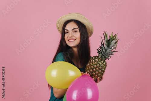 Smiling woman in a hat poses with colorful balloons and a pineapple © IVASHstudio