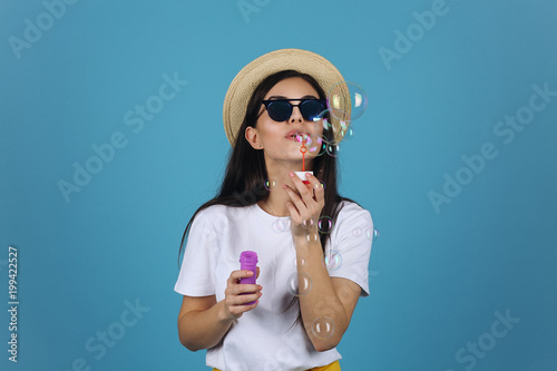 Laughing brunette girl in summer hat and sunglasses has fun with soap balloons
