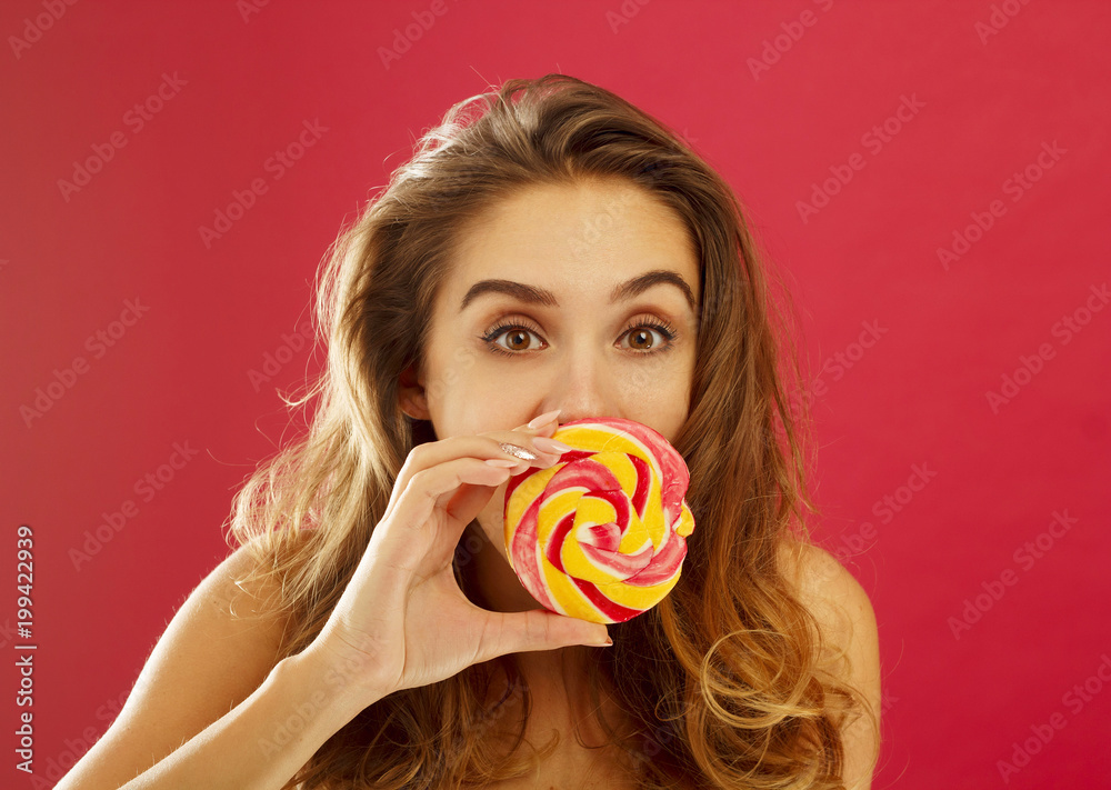 Portrait of a happy girl holding sweet candy over red background