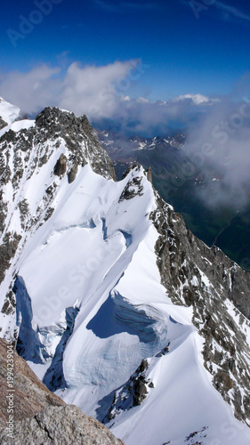 narrow and exposed summit ridge with a giant wave cornice on the way to the top of a peak in the Alps