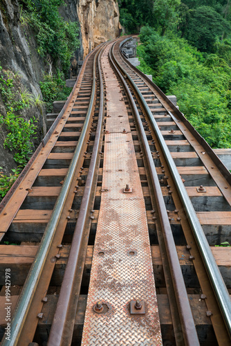 Old railroad tracks on bridge beside cliff rock