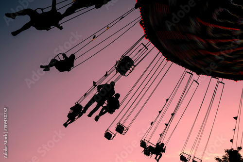 silhouettes of people on swing carousel against purple evening summer sky photo