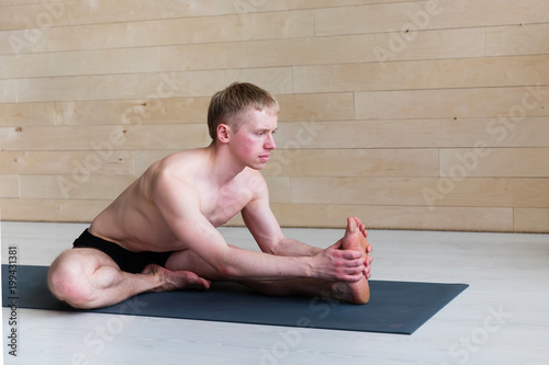 Sporty man doing Paschimottasana pose on yoga class photo